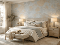 A beautifully styled bedroom featuring a bed dressed in cream and light blue-gray bedding, set against a textured light blue and beige wallpaper. The room is symmetrically arranged with matching wooden nightstands, lit table lamps, a decorative bench at the foot of the bed, and a large window with sheer curtains on the left.