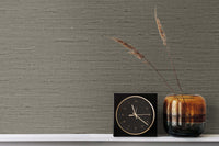 Black faux grasscloth wallpaper with a black and gold clock and ombre bronze vase with wheat strands