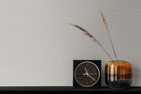 grey grasscloth wallpaper with a black and gold clock next to an ombre gold vase with two strands of wheat