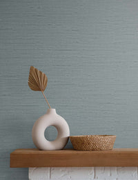 light blue grasscloth wallpaper with a white circular case and a single golden leaf next to a brown wicker basket atop a white brick and brown wood mantle piece