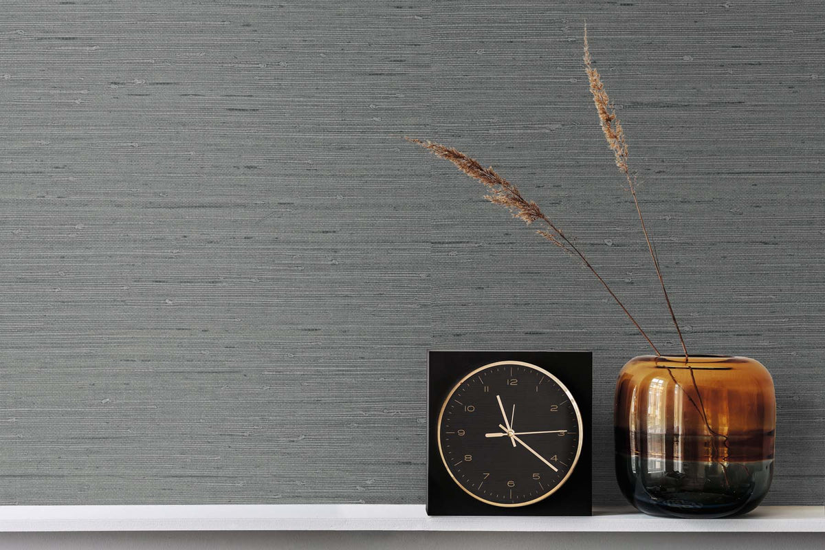 Dark Grey Grasscloth wallpaper with a gold and black clock next to a brown vase with strands of wheat inside it