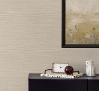 woven beige faux grasscloth wallpaper with a black framed golden poster of wisteria. A black bureau with a sandy and white colored clock, a terrazzo tray with a brown glass paper weight, next to a white and black pinstripe mug.