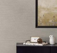 beige faux grasscloth wallpaper with a black framed golden poster of wisteria. A black bureau with a sandy and white colored clock, a terrazzo tray with a brown glass paper weight, next to a white and black pinstripe mug.