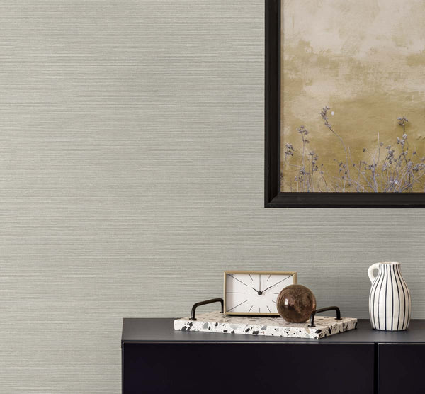light gray grasscloth wallpaper with a black framed golden poster of wisteria. A black bureau with a sandy and white colored clock, a terrazzo tray with a brown glass paper weight, next to a white and black pinstripe mug.